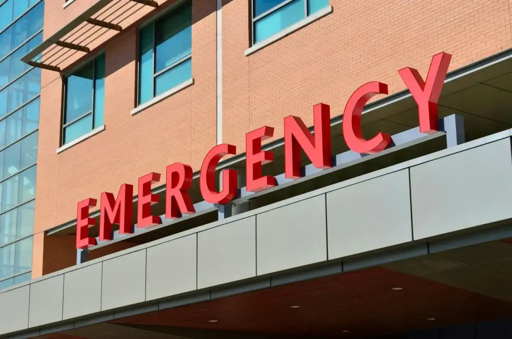 Large red EMERGENCY letters on the exterior facade of a hospital emergency room entrance.