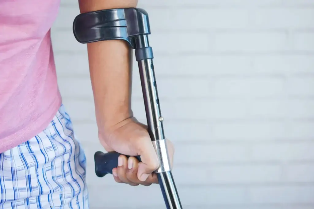 An injured person in a pink shirt gripping a metal forearm crutch while recovering from a personal injury.